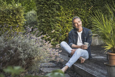 Thoughtful man holding coffee cup sitting on porch - UUF30281