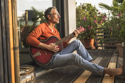 Mann spielt Gitarre auf Veranda sitzend - UUF30282