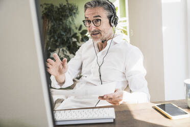 Geschäftsmann, der ein Headset trägt und über einen Videoanruf im Büro zu Hause spricht - UUF30309