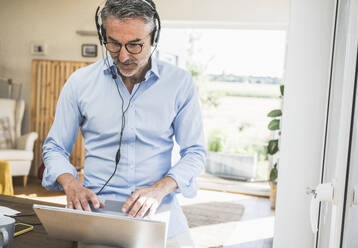 Geschäftsmann mit Headset bei der Arbeit am Laptop im Home Office - UUF30335