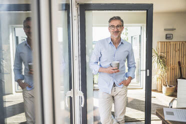 Lächelnder Geschäftsmann mit Kaffeetasse in seinem Büro - UUF30347