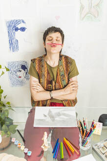 Künstlerin hält Bleistift zwischen Nase und Lippe am Tisch - MGRF01050