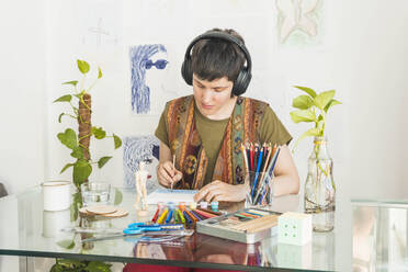 Artist wearing wireless headphones and painting at table - MGRF01054