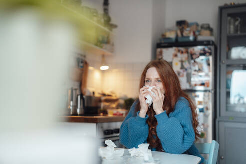 Sick woman blowing nose on tissue at home - KNSF09878