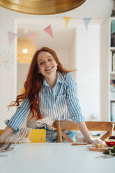 Smiling woman leaning on dining table at home - KNSF09886