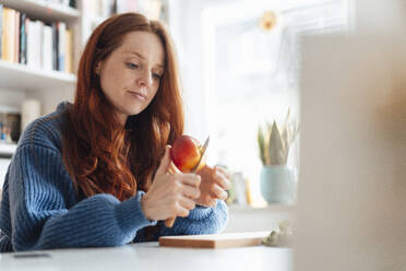 Woman cutting apple with knife in kitchen at home - KNSF09895