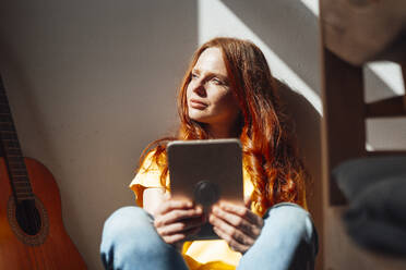 Kontemplative rothaarige Frau mit Tablet-PC sitzend - KNSF09920