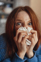 Redhead woman blowing nose on tissue paper at home - KNSF09925