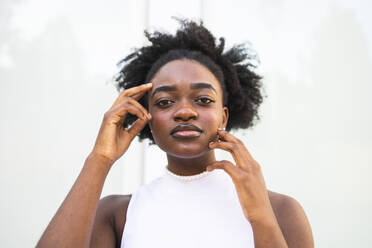 Portrait of young African American female in afro hairdo with white armless top standing looking at camera against white background in daylight - ADSF47122