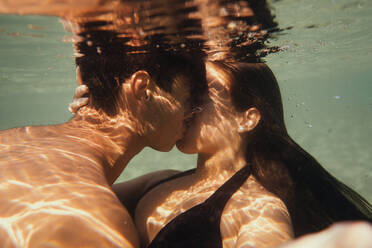 Side view of young couple kissing under seawater with closed eyes - ADSF47154