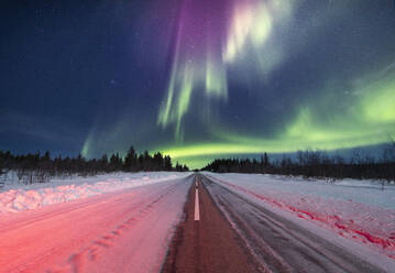 Long road covered with snow under spectacular aurora borealis in starry sky during winter in Lapland Norway - ADSF47179