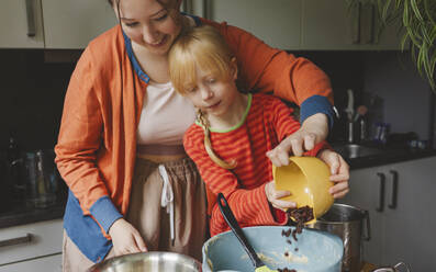 Teenage girl and her younger sister putting raisins in mixing bowl at kitchen - IHF01693