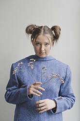 Teenager-Mädchen trägt blauen Blazer verkehrt herum und hält Blumen vor einer Wand - IHF01696