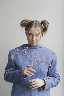 Teenager-Mädchen trägt blauen Blazer verkehrt herum und hält Blumen vor einer Wand - IHF01696
