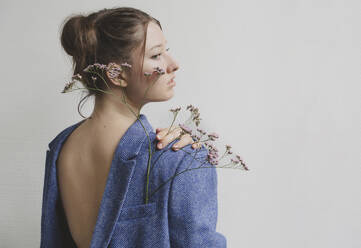 Teenager-Mädchen trägt blauen Blazer rückwärts mit Blumen in der Tasche an der Wand - IHF01698