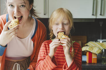 Teenage girl and her younger sister eating baked muffins in kitchen - IHF01702