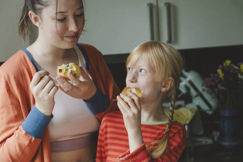 Blondes Mädchen isst Muffins mit älterer Schwester in der Küche zu Hause - IHF01703