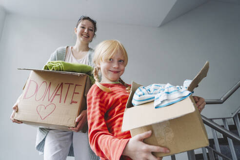 Lächelnde Schwestern mit Kleiderspenden in Kartons, die die Treppe hinuntergehen - IHF01705