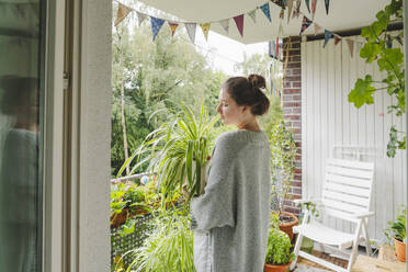 Teenage girl holding potted plant standing on balcony at home - IHF01714