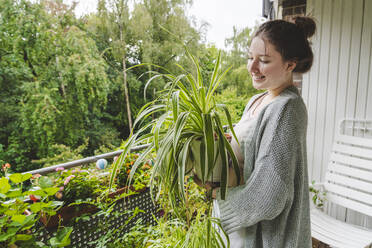 Smiling teenage girl with potted plant standing on balcony - IHF01715