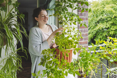 Glückliches Teenager-Mädchen mit Topf-Tomatenpflanze auf dem Balkon - IHF01720