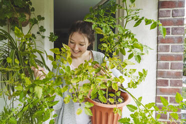 Happy teenage girl with potted plants on balcony - IHF01723
