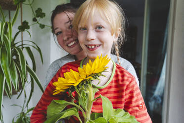 Teenager-Mädchen mit blonder Schwester hält Sonnenblume auf Balkon - IHF01729