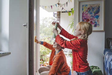 Blond girl spraying water and elder sister cleaning door of balcony - IHF01731