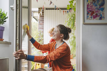 Smiling teenage girl cleaning door with sister in background at home - IHF01732