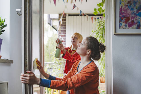 Mädchen sprüht Wasser und ältere Schwester reinigt Balkontür - IHF01733