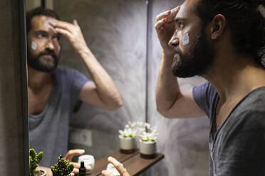 Man applying moisturizer on face in front of mirror - JPTF01320