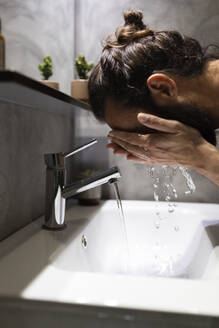 Man washing face in bathroom sink - JPTF01324