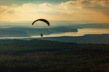 Aerial view of single paramotor pilot flying over forest near a reservoir lake on the northeastern coast of Istanbul, Turkey. - AAEF21920