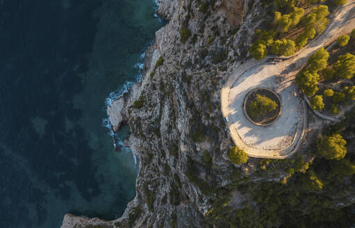 Luftaufnahme eines Kreisverkehrs auf einer Klippe in Küstennähe bei Sonnenuntergang, Cala Moraig, Zona Encinas, Cumbre del Sol, Alicante, Spanien. - AAEF22086