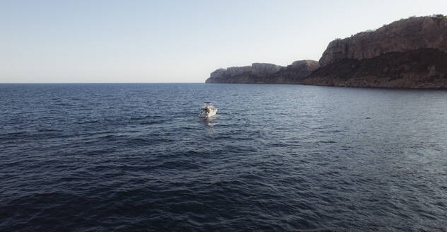 Aerial view of a small boat floating in a tranquil sea with clear blue water, Zona Encinas, Cumbre del Sol, Alicante, Spain. - AAEF22087