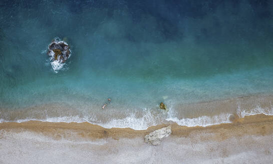 Luftaufnahme von zwei Männern, die in kristallklarem, von der Sonne beleuchtetem Wasser an einem leeren Strand schwimmen, Cala Moraig, Zona Encinas, Cumbre del Sol, Alicante, Spanien. - AAEF22090