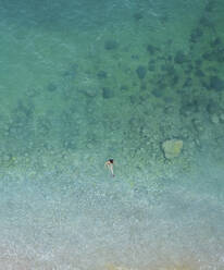 Luftaufnahme einer Frau, die in kristallklarem Wasser schwimmt, das vom Sonnenlicht beleuchtet wird, Cala Moraig, Zona Encinas, Cumbre del Sol, Alicante, Spanien. - AAEF22091