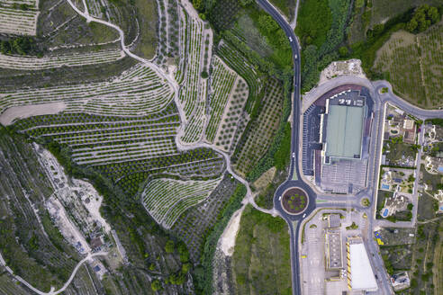 Luftaufnahme einer Serpentinenstraße und eines modernen Gebäudekomplexes in der Nähe von grünen landwirtschaftlichen Feldern, Zona Encinas, Cumbre del Sol, Alicante, Spanien. - AAEF22105