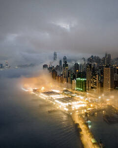 Aerial view of Hong Kong downtown along the harbour facing the bay with low clouds at night. - AAEF22179