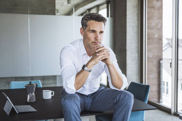 Contemplative businessman sitting on desk - UUF30357
