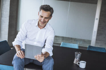 Lächelnder Geschäftsmann mit Tablet-PC auf dem Schreibtisch im Büro - UUF30361