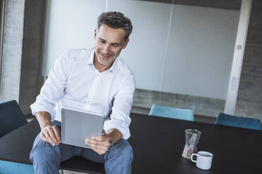 Smiling businessman using tablet PC on desk in office - UUF30361