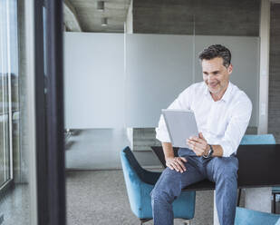 Smiling businessman using tablet PC on desk - UUF30362