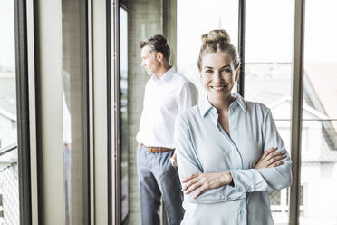 Happy businesswoman with colleague standing in background - UUF30380