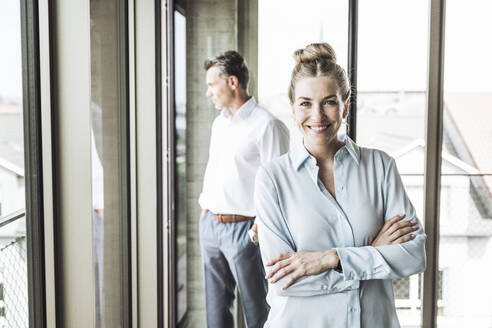 Happy businesswoman with colleague standing in background - UUF30380