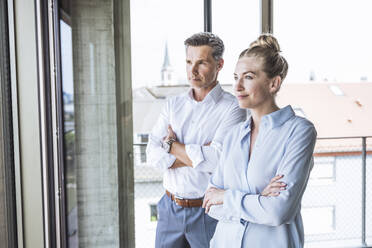 Thoughtful businessman and businesswoman standing with arms crossed - UUF30383