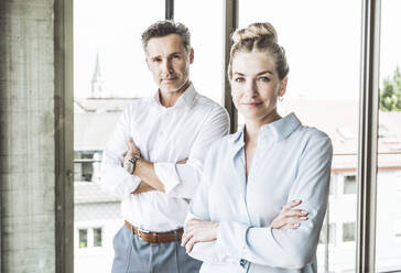 Smiling businessman and businesswoman standing with arms crossed - UUF30384
