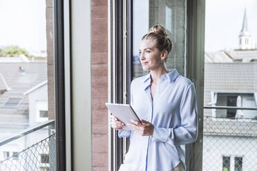 Thoughtful businesswoman standing with tablet PC in office - UUF30387