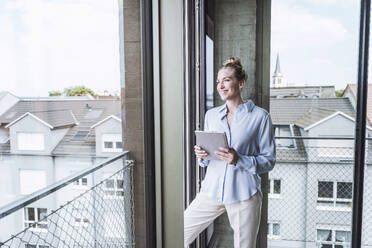 Happy businesswoman standing with tablet PC in office - UUF30390