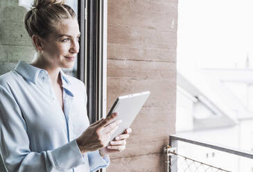 Contemplative businesswoman standing with tablet PC in office - UUF30391